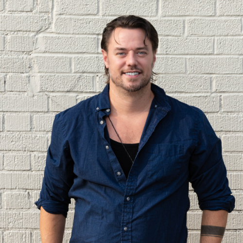 male in button down shirt in front of brick wall