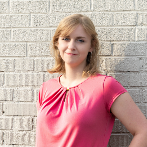 female with hand on left hip standing in front of a white brick wall