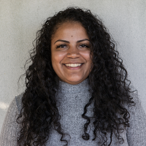 female with curly hair standing in front of a wall