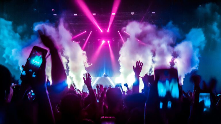 crowd of people with hands raised in a club with laser lights and smoke