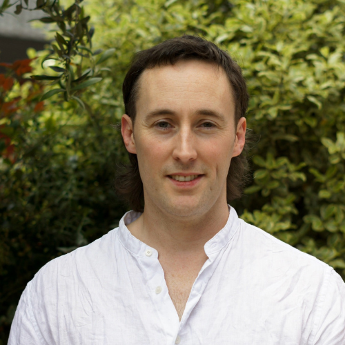 Male standing in front of a green tree smiling