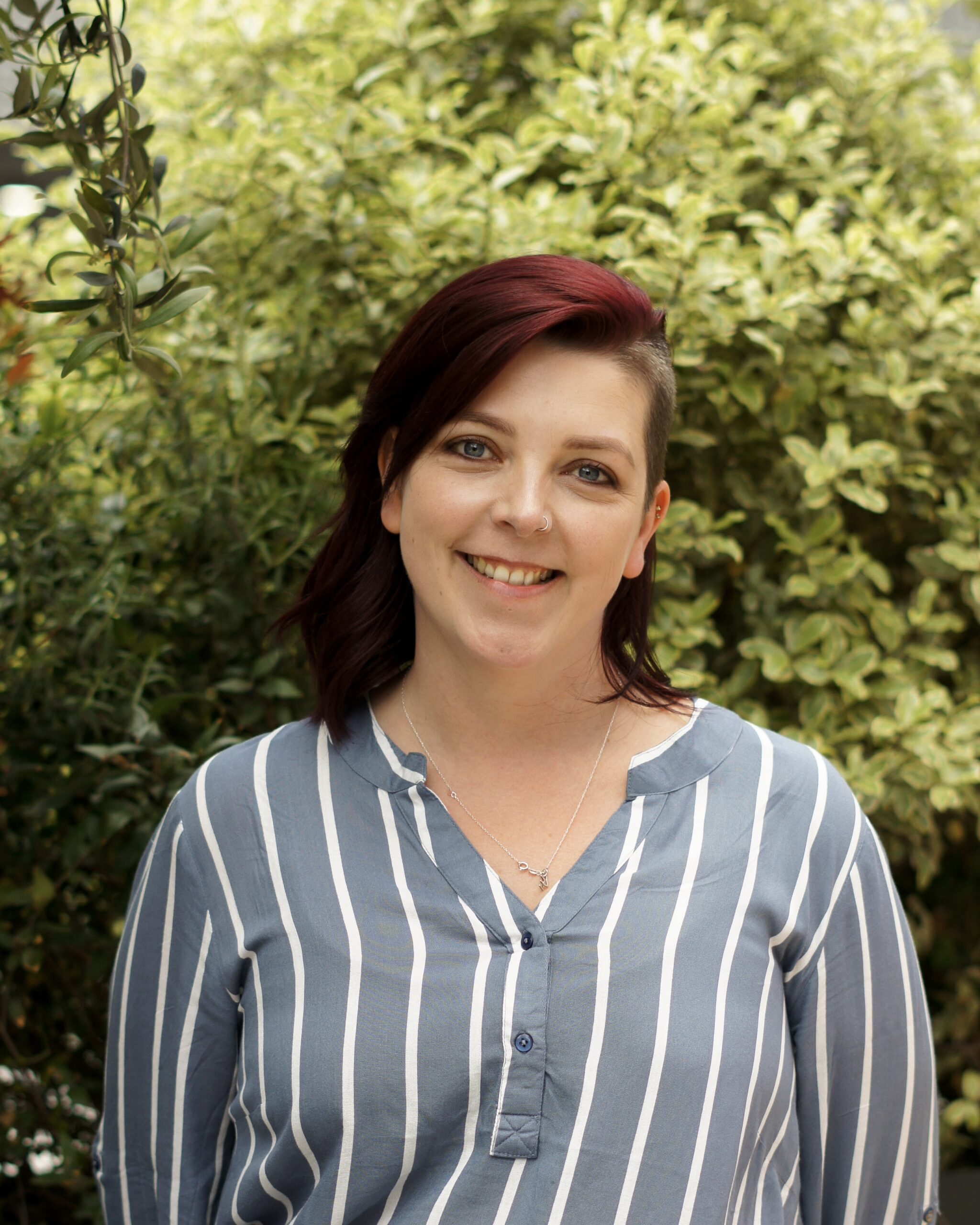 female smiling standing in front of a tree with a verticals striped shirt