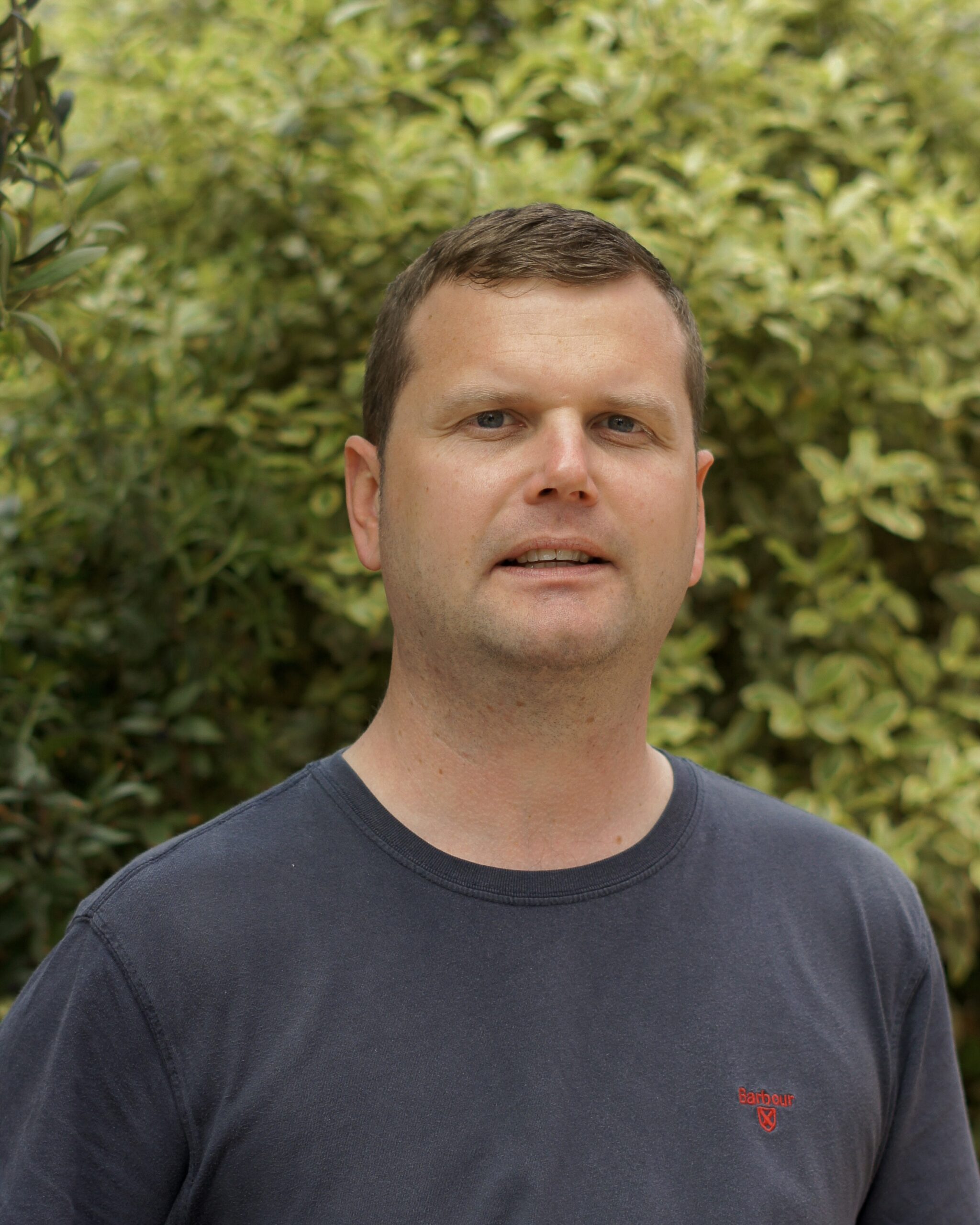 Male from shoulders up standing in front of a tree with grey shirt