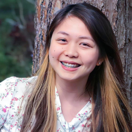 Smiling female with long hair, standing in front of a tree trunk