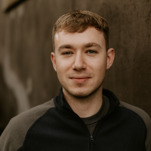 Male with green shirt standing in front of a dark wall